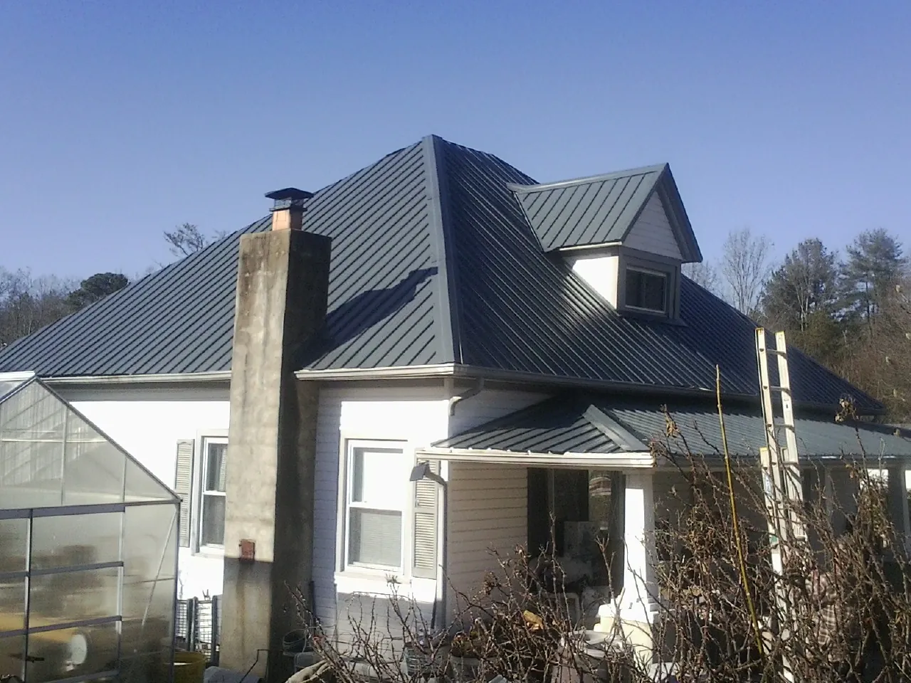 Dark blue standing seam metal roof on a white farmhouse with dormer — Slate & Tile Roof Repair by Roofing Brothers in Edgar