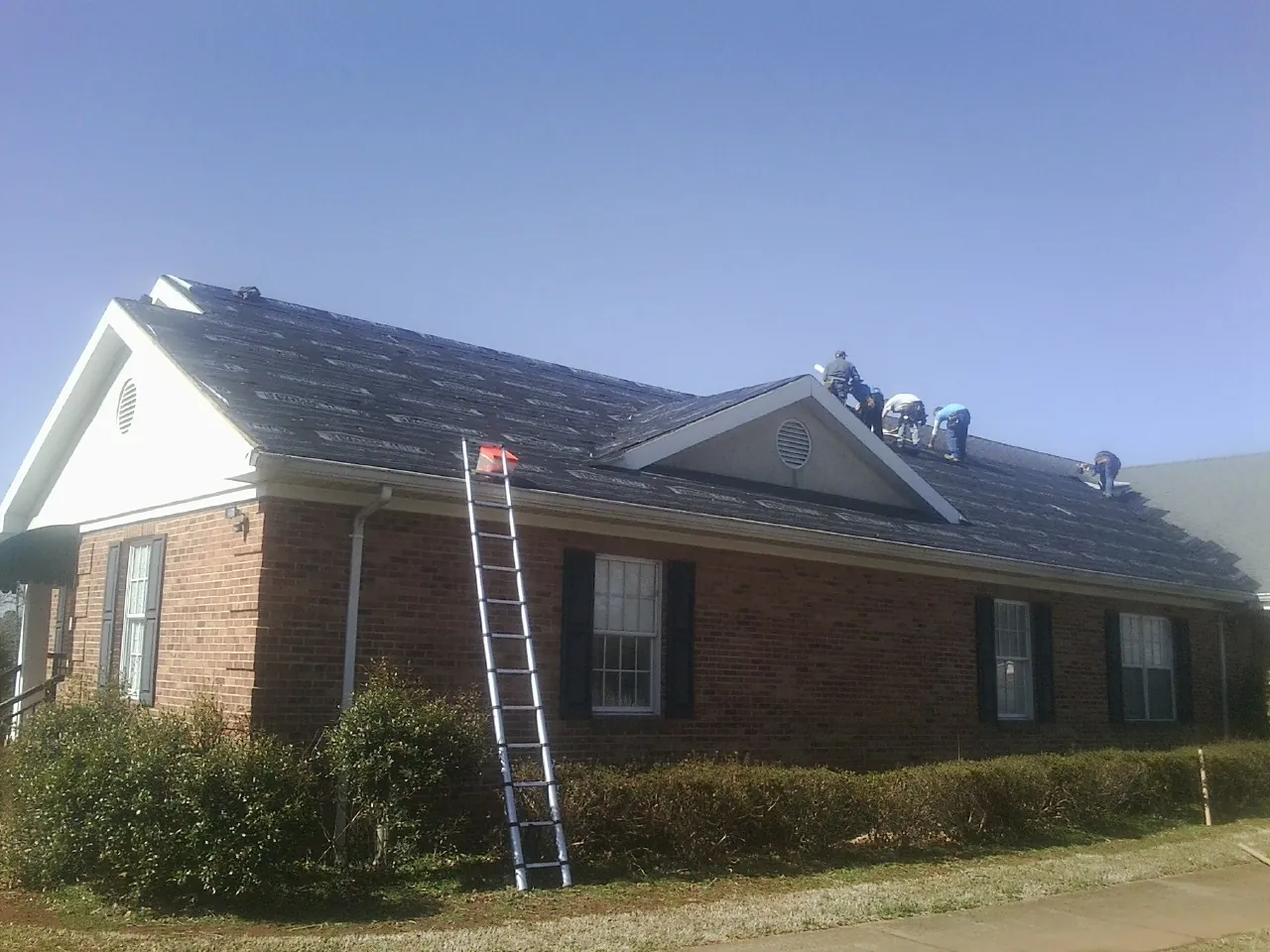 Crew tearing shingles off a brick ranch roof with a ladder set — Metal Roof Repair work by our crew in Edgar
